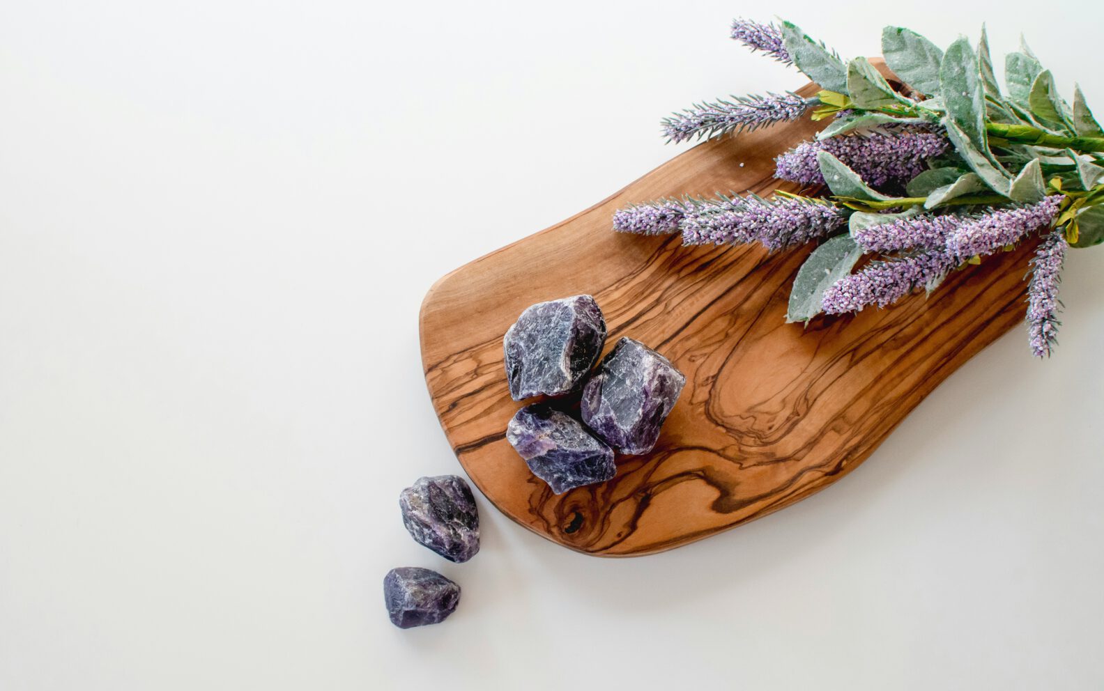 purple crystals on a wooden board next to fresh lavender and sage leaves